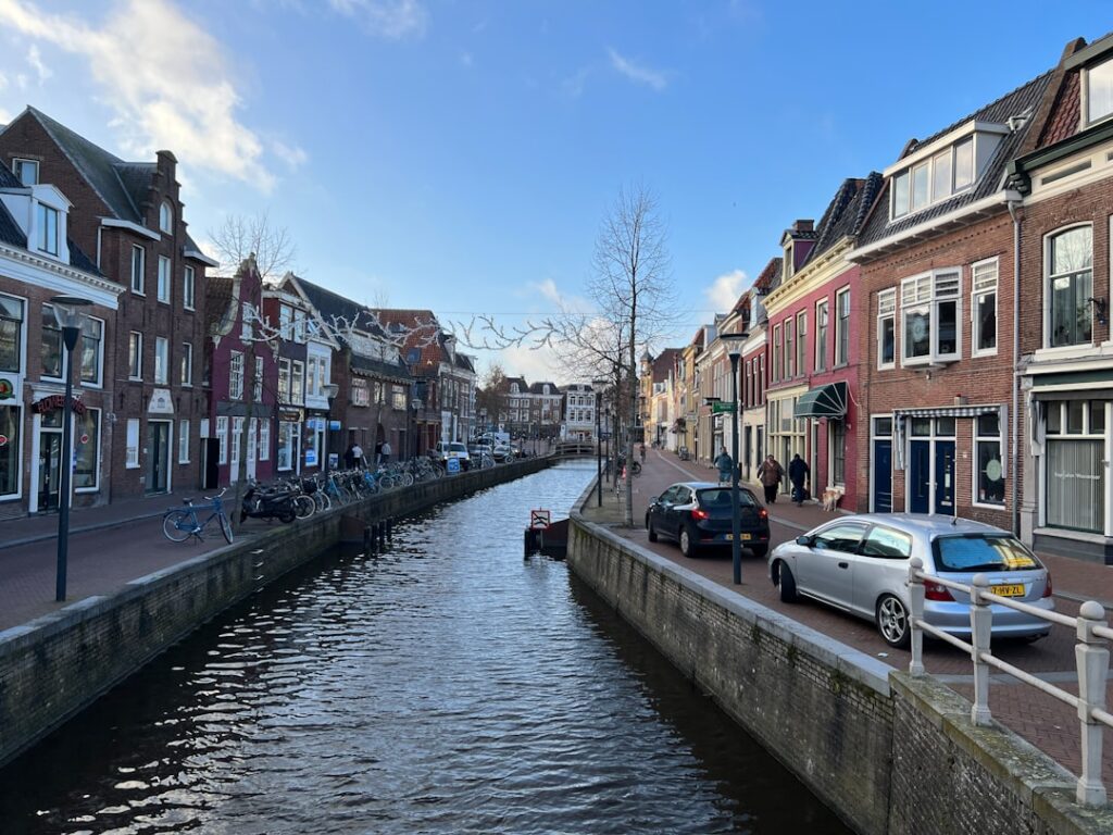 A tranquil canal scene is disrupted by the presence of parked cars, highlighting the unique urban character of Leeuwarden's Nieuwekade. The juxtaposition of water and vehicles creates a striking visual contrast.