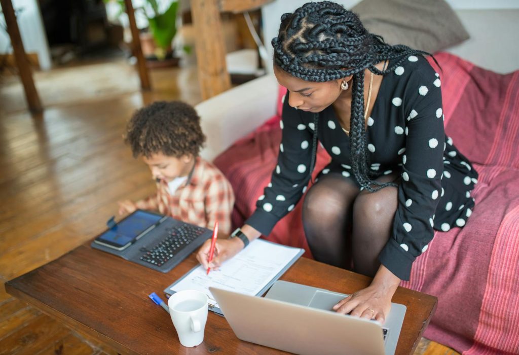 Photo by Kampus Production Mother multitasking with work and child at home, showcasing modern parenting.