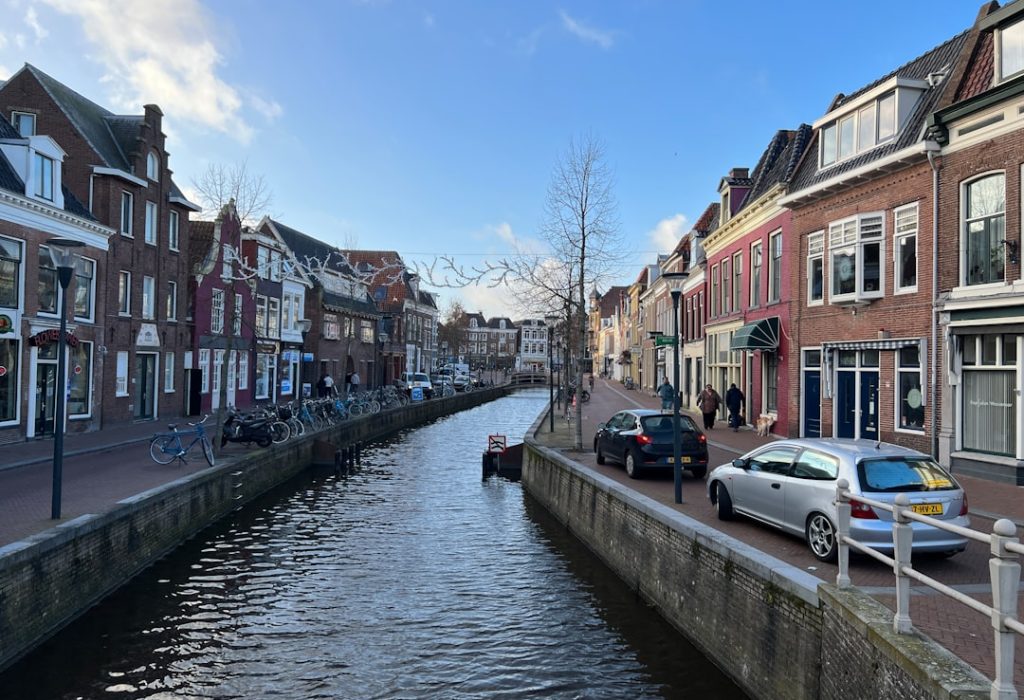 A tranquil canal scene is disrupted by the presence of parked cars, highlighting the unique urban character of Leeuwarden's Nieuwekade. The juxtaposition of water and vehicles creates a striking visual contrast.